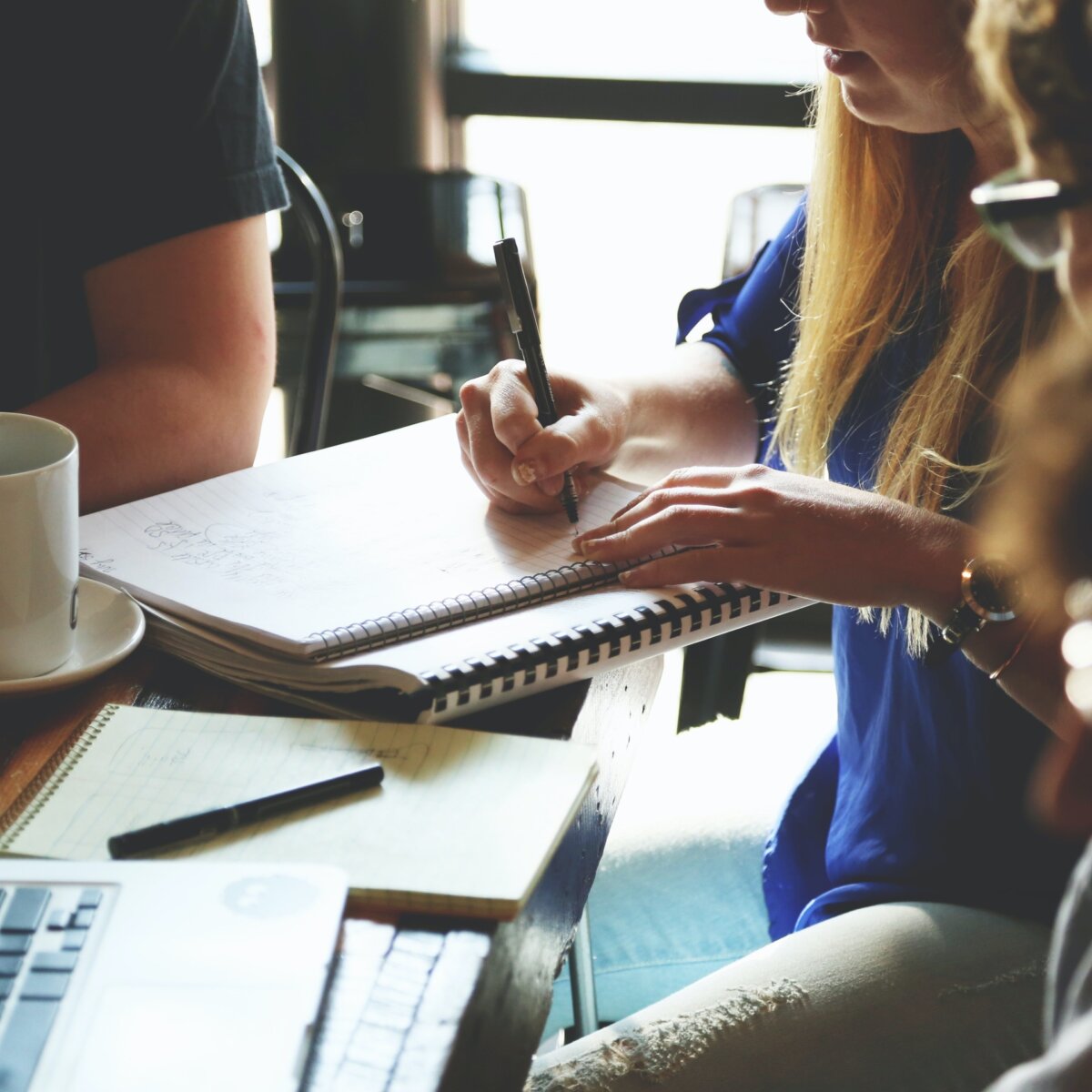 Group of people with notebooks, laptops, and coffee working together at table