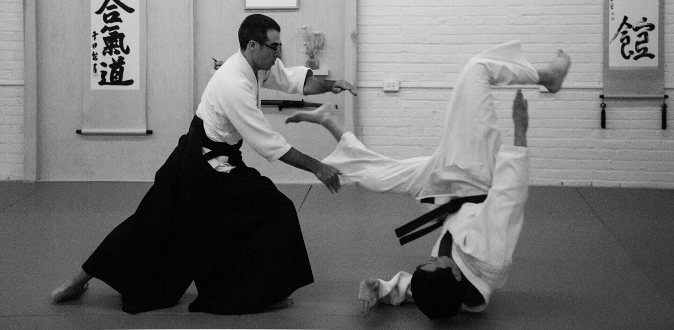 Sensei demonstrating a throwing technique to a student who is mid roll as they take the fall.