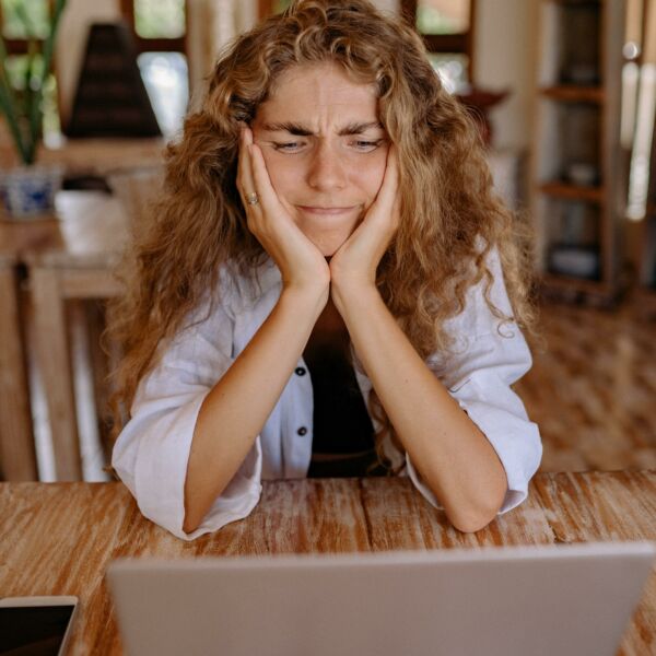 Woman holding her face with her hands, eyes squinting, while staring at her laptop