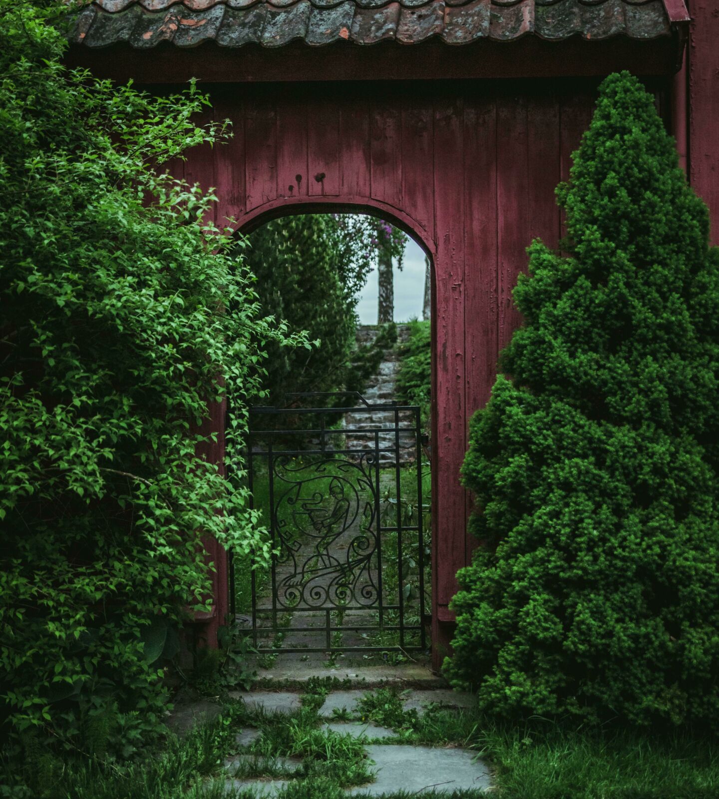 Garden gate with a stone path leading up to it and that is surrounded by vegetation.
