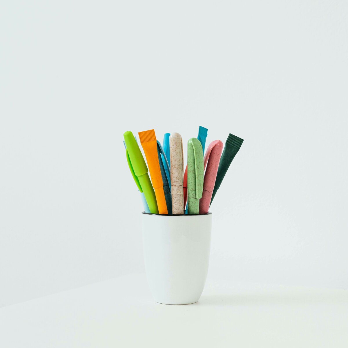 Colorful markers and pens arranged in a white ceramic cup against a clean white background, demonstrating the visual impact of strategic white space in composition and design.